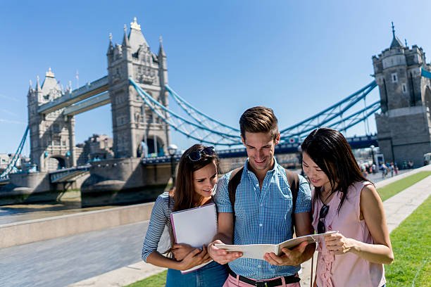 Happy group of students in London studying outdoors near Tower Bridge and smiling